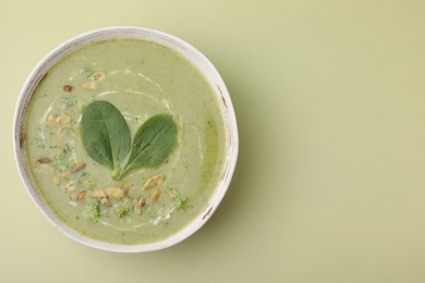 Photo of Delicious broccoli cream soup with basil and pumpkin seeds on green background, top view. Space for text