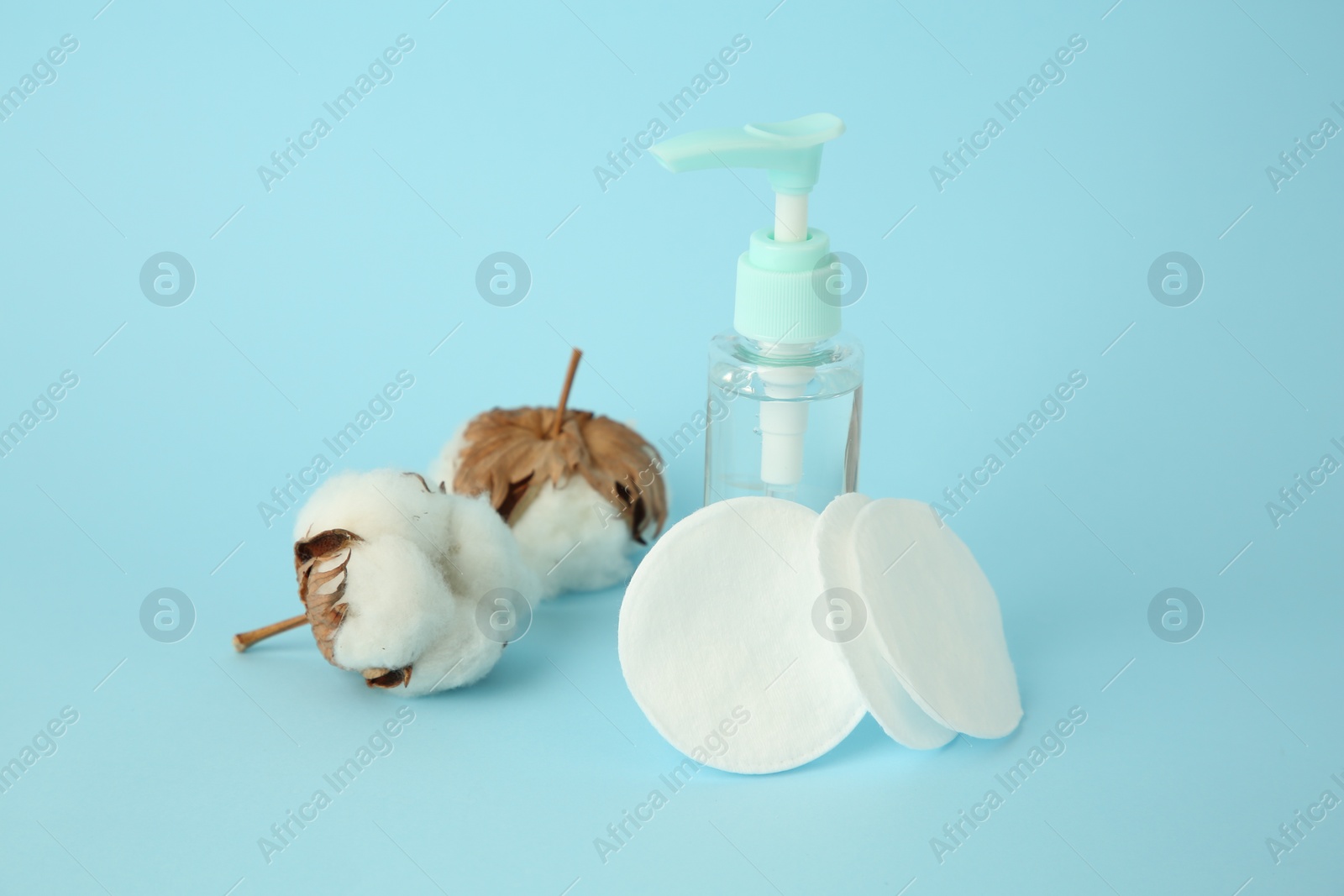 Photo of Cosmetic product, cotton pads and flowers on light blue background, closeup