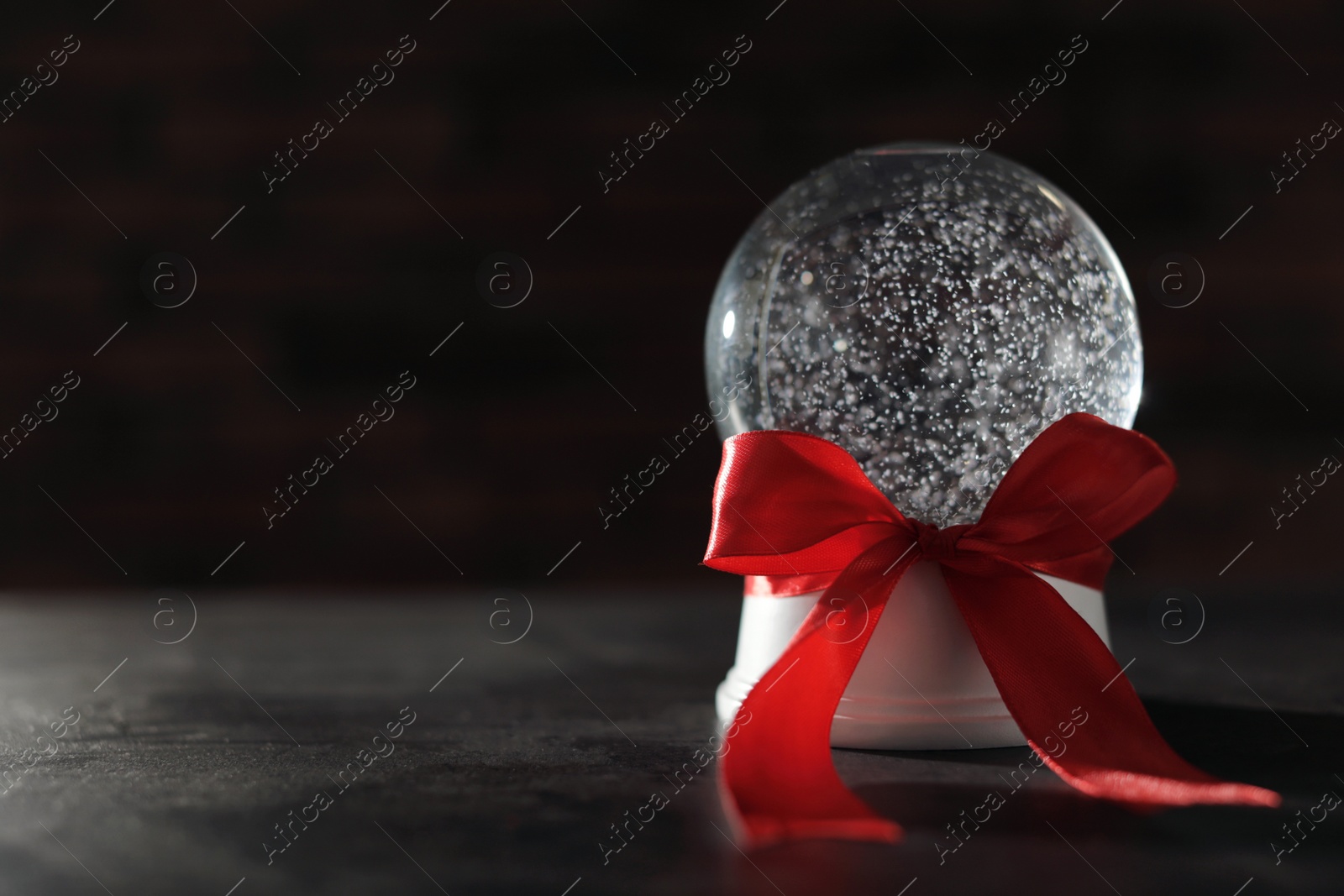 Photo of Christmas snow globe with red bow on dark background. Space for text