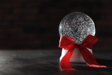 Christmas snow globe with red bow on dark background. Space for text