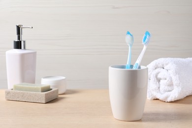 Photo of Plastic toothbrushes in holder, soap, dispenser and towel on wooden table