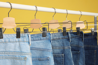 Photo of Rack with different jeans on yellow background, closeup