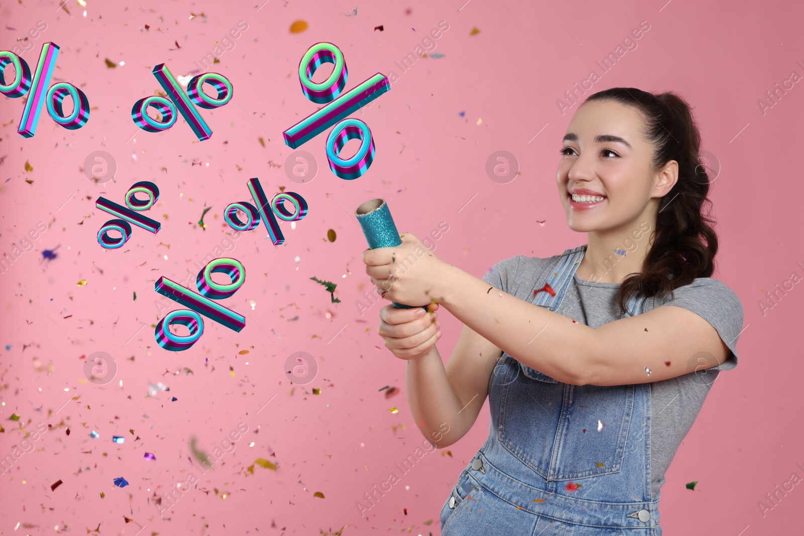 Image of Discount offer. Happy young woman blowing up party popper on pink background. Confetti and percent signs in air