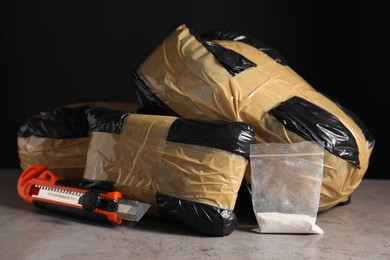 Photo of Smuggling, drug trafficking. Packages with narcotics and utility knife on grey table