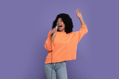 Beautiful woman with microphone singing on violet background