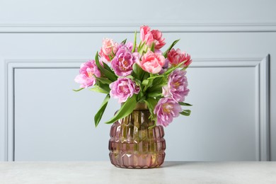 Photo of Beautiful bouquet of colorful tulip flowers on white table near light grey wall