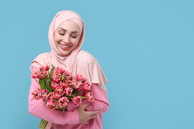 Photo of Happy woman in hijab with beautiful bouquet on light blue background. Space for text