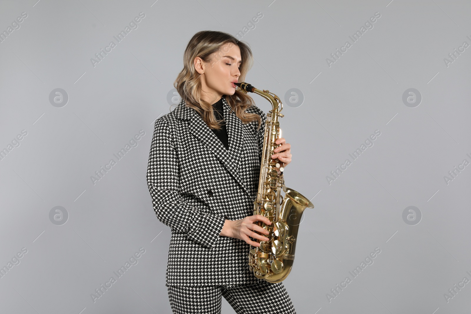 Photo of Beautiful young woman in elegant suit playing saxophone on grey background