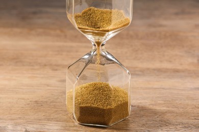 Photo of Hourglass with flowing sand on wooden table, closeup
