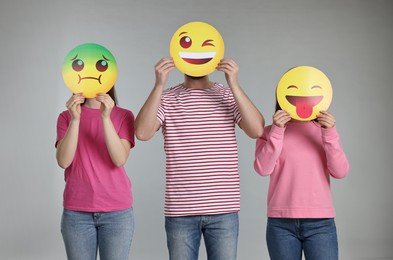 People covering faces with emoticons on grey background