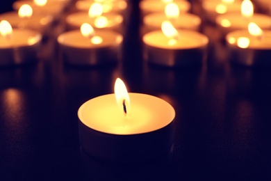 Photo of Wax candle burning on table in darkness, closeup