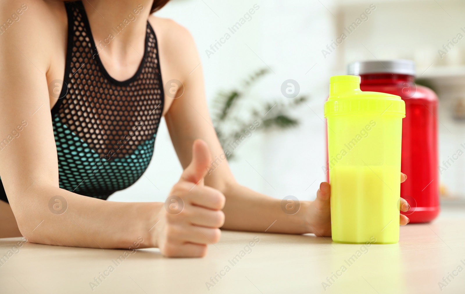 Photo of Young woman with bottle of protein shake at table in kitchen, closeup view