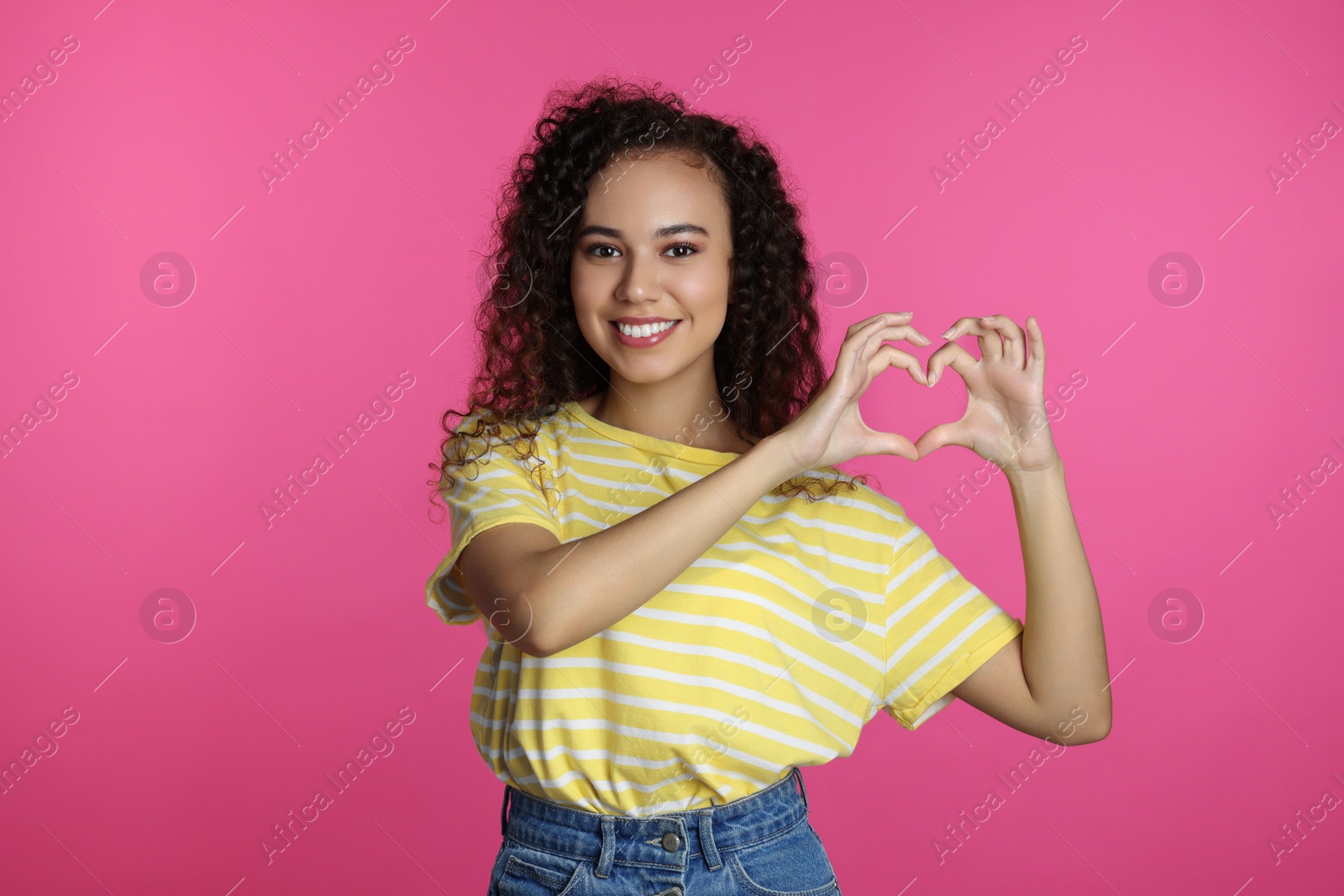 Photo of Happy young African-American woman making heart with hands on pink background