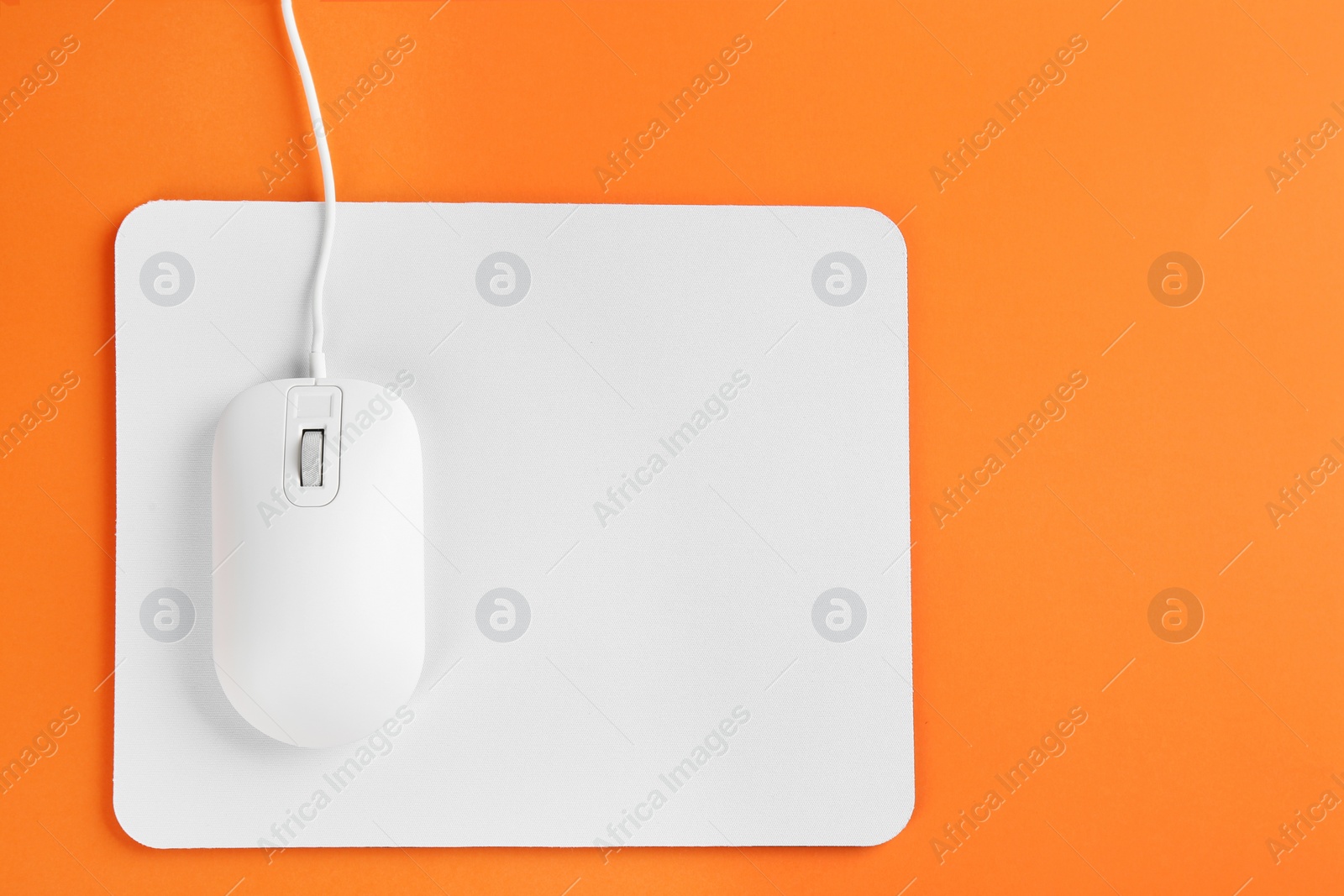 Photo of Modern wired optical mouse and pad on orange background, top view. Space for text