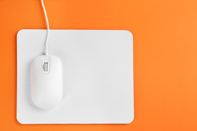 Photo of Modern wired optical mouse and pad on orange background, top view. Space for text