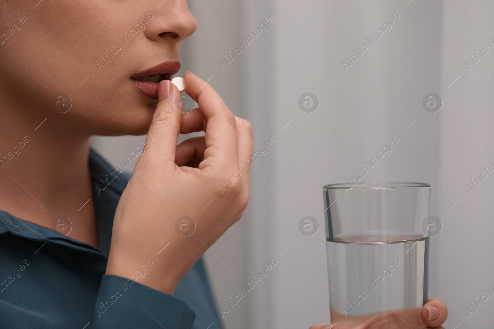 Photo of Woman with glass of water taking antidepressant pill on light background, closeup