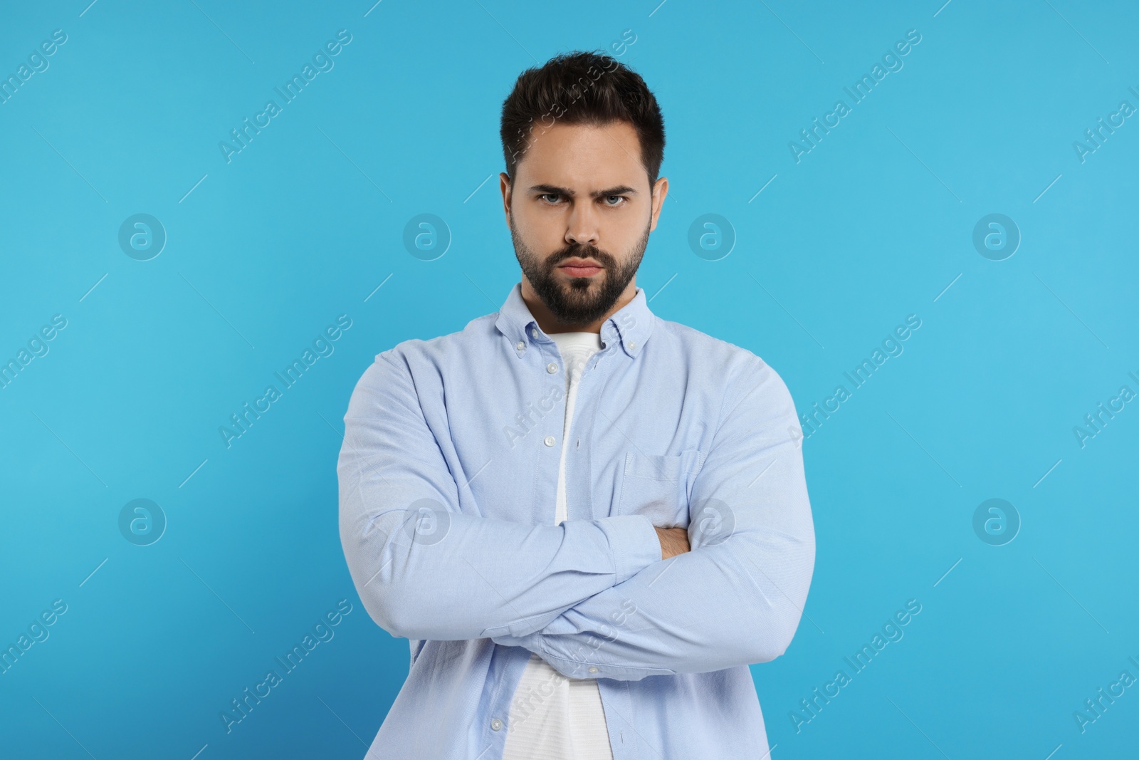 Photo of Portrait of resentful man with crossed arms on light blue background