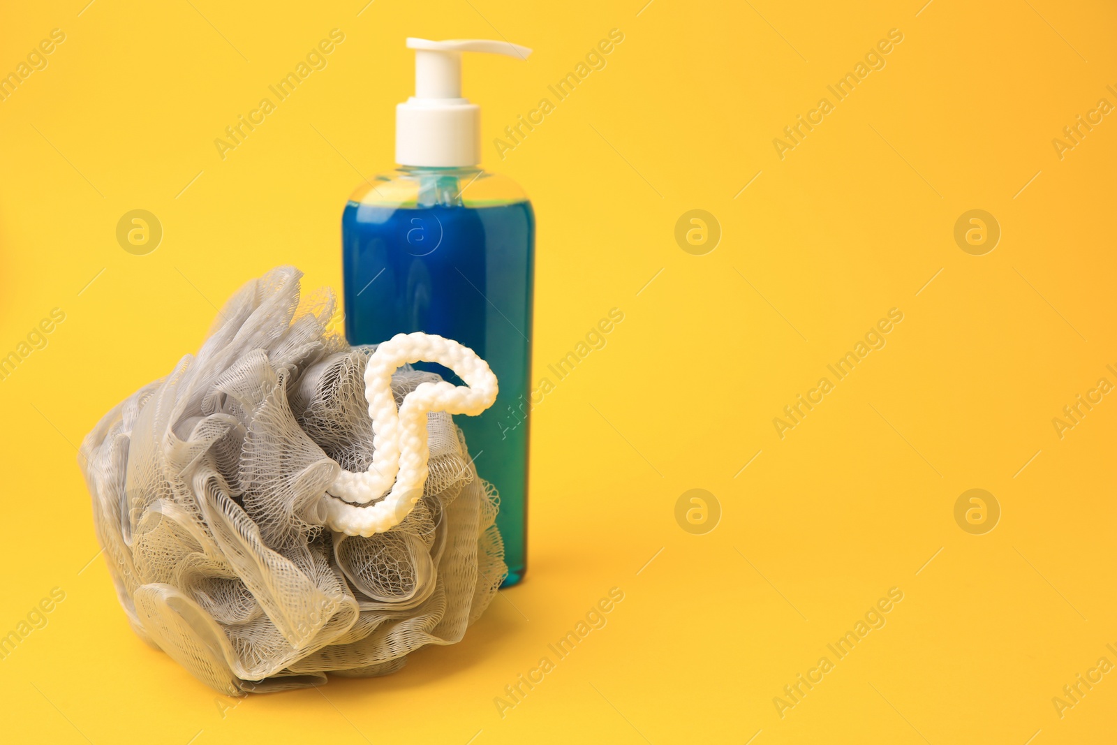 Photo of Grey shower puff and bottle of cosmetic product on yellow background, space for text