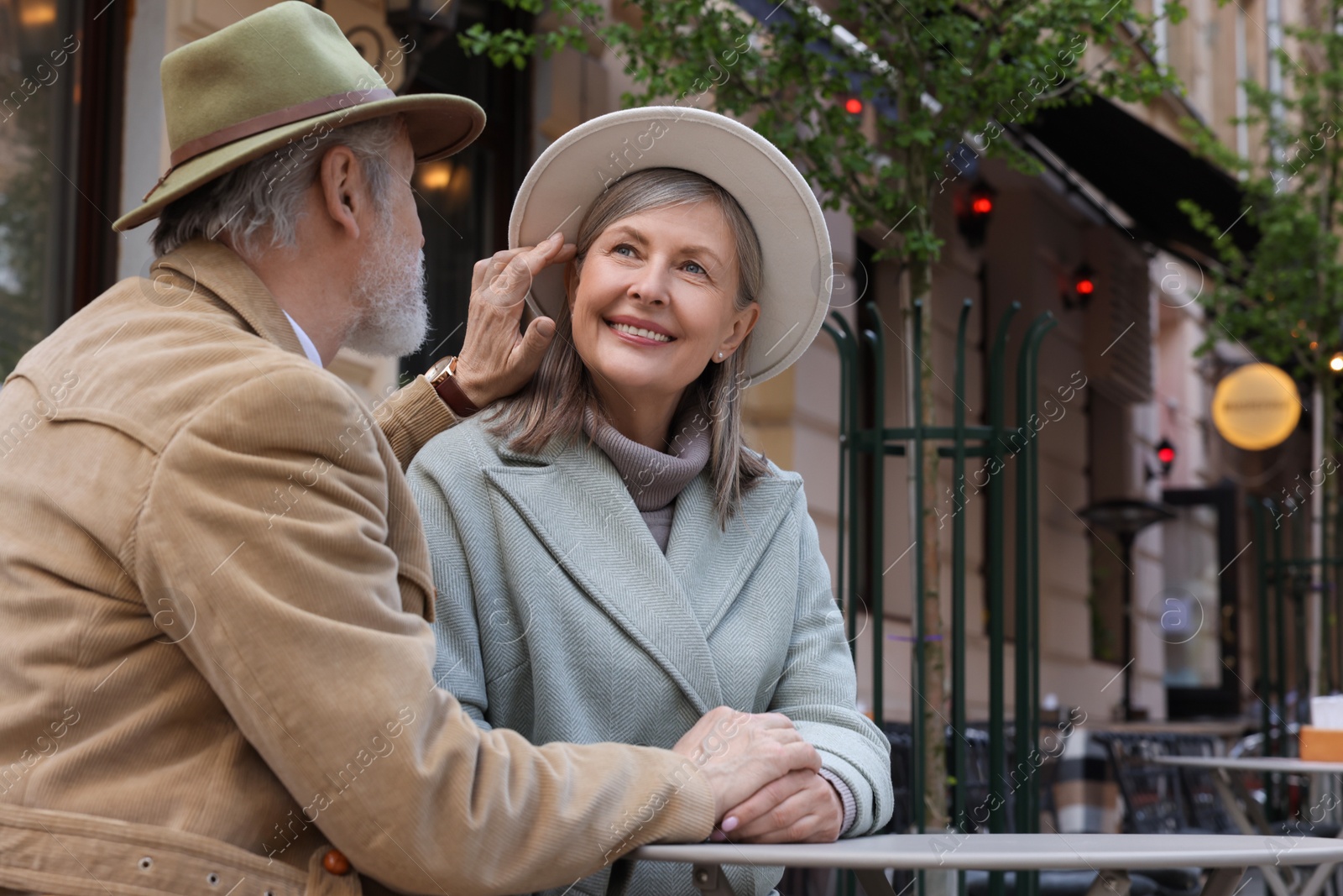 Photo of Portrait of affectionate senior couple sitting in outdoor cafe, space for text