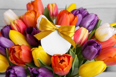 Bouquet of beautiful colorful tulips with blank card on white wooden background, closeup. Birthday celebration