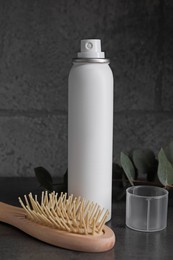 Dry shampoo spray, eucalyptus branch and hairbrush on dark table near grey wall