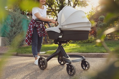 Photo of Happy mother with baby in stroller walking in park on sunny day, closeup