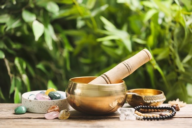 Photo of Composition with tibetan singing bowl and different gemstones on wooden table outdoors. Sound healing