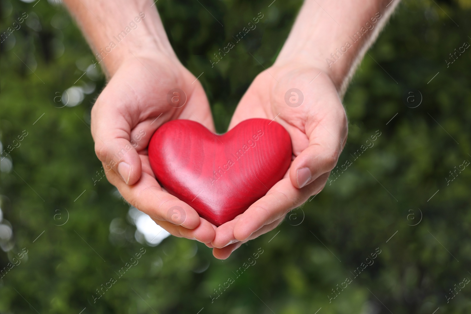 Photo of Young man holding red heart on blurred green background, closeup. Donation concept