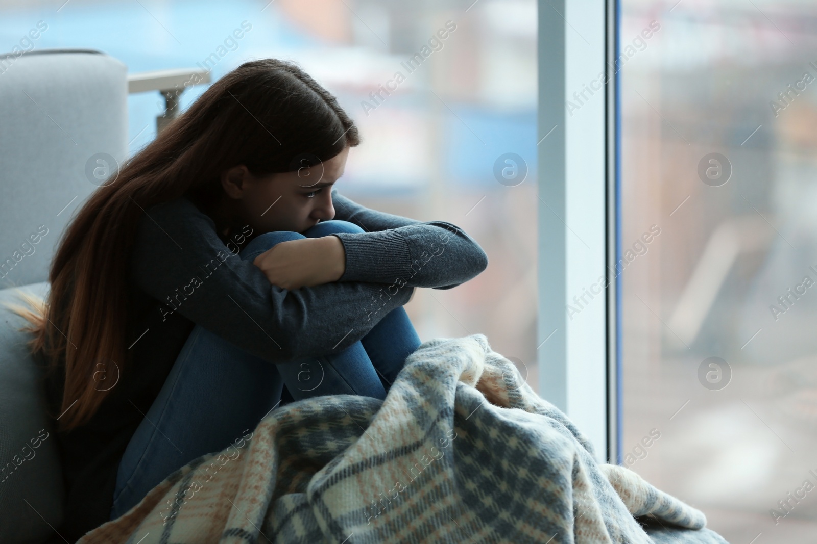 Photo of Upset teenage girl sitting at window indoors. Space for text