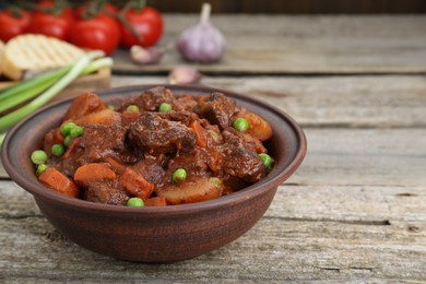 Photo of Delicious beef stew with carrots, peas and potatoes on wooden table, closeup. Space for text