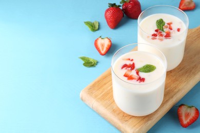 Photo of Tasty yogurt in glasses and strawberries on light blue wooden table. Space for text