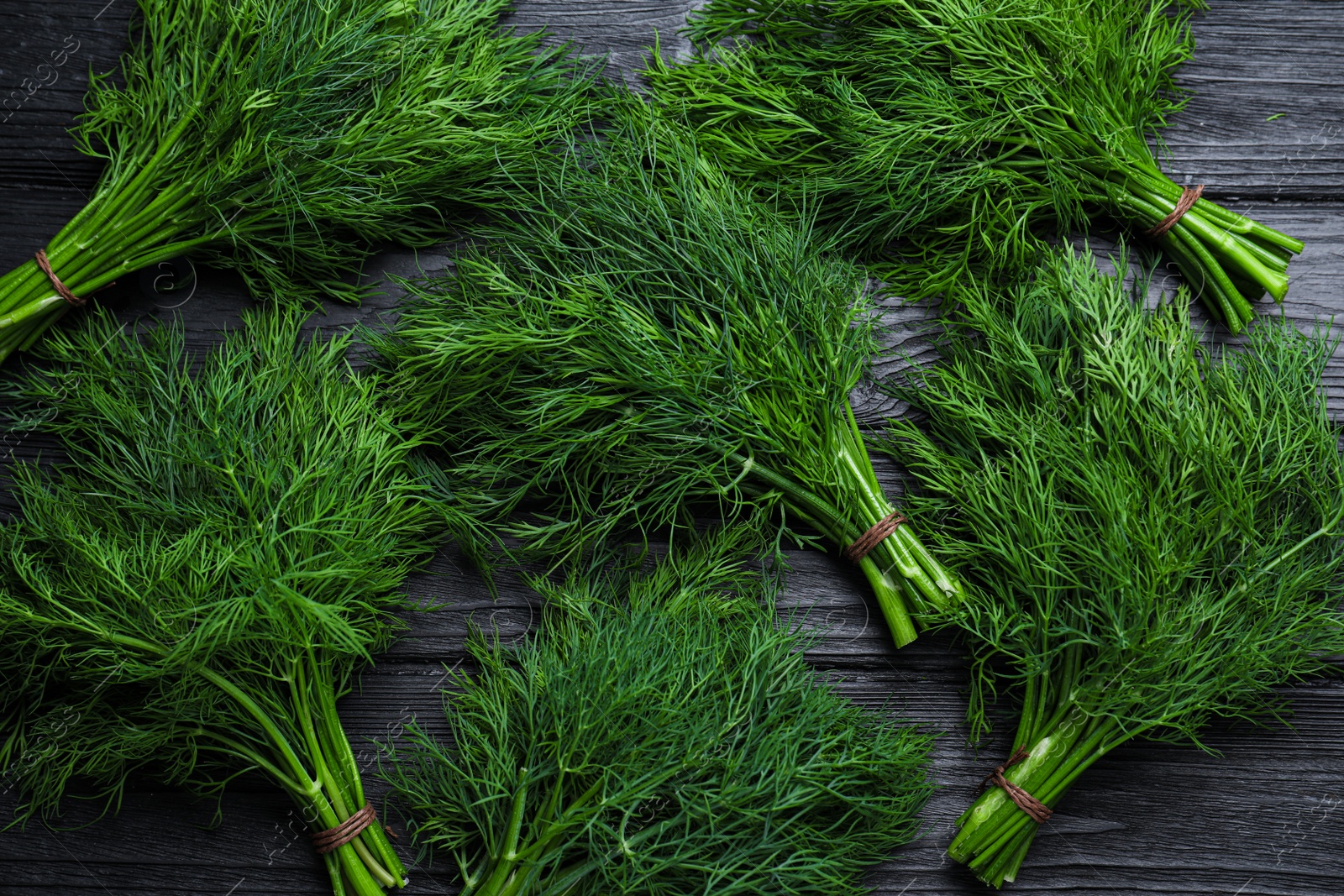 Photo of Bunches of fresh dill on black wooden table, flat lay