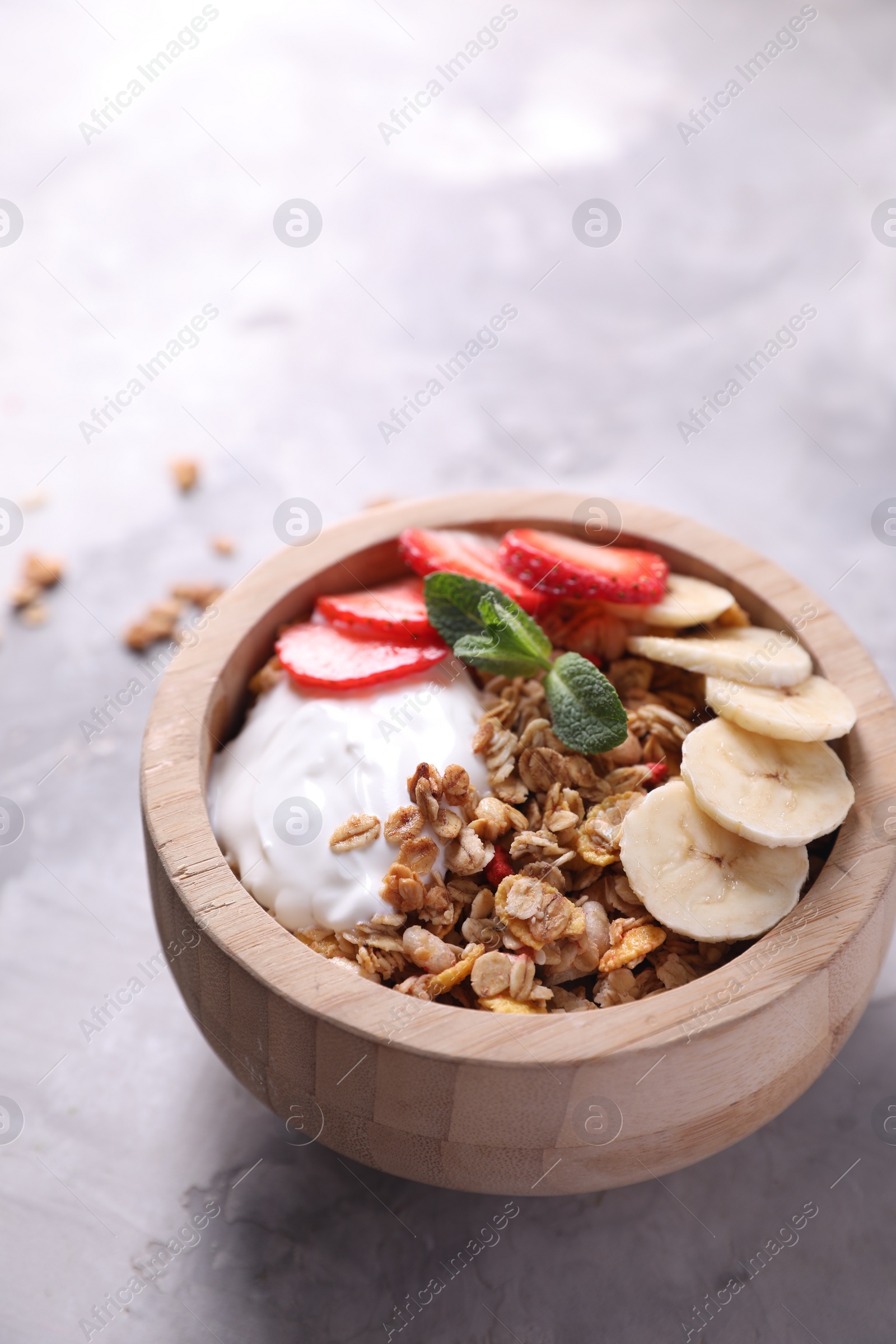 Photo of Tasty granola with yogurt, banana and strawberry in bowl on gray textured table, closeup