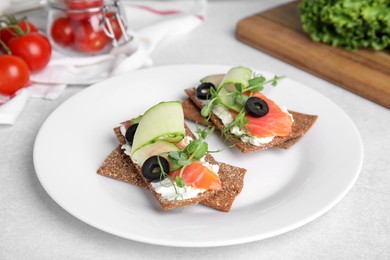Photo of Tasty rye crispbreads with salmon, cream cheese and vegetables served on light grey table