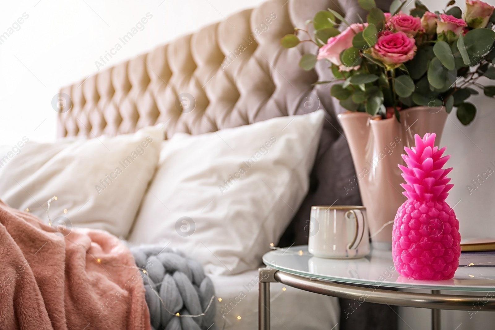 Photo of Pineapple shaped candle, vase with flowers and cup of coffee on bedside table in room