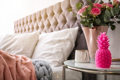 Pineapple shaped candle, vase with flowers and cup of coffee on bedside table in room