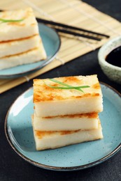Photo of Delicious turnip cake with herb on black table, closeup