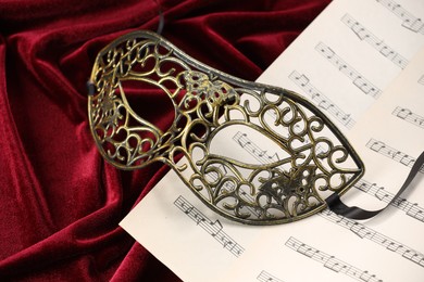 Elegant face mask and music sheets on red fabric. Theatrical performance