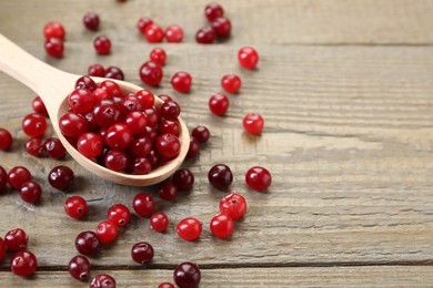 Photo of Spoon with fresh ripe cranberries on wooden table, closeup. Space for text