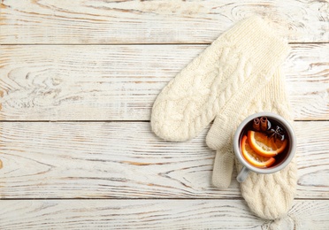 Photo of Cup of hot winter drink and warm knitted mittens on wooden background, top view with space for text. Cozy season