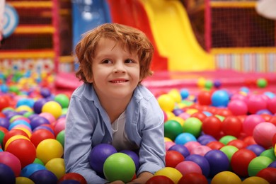 Photo of Happy little boy lying on colorful balls in ball pit, space for text