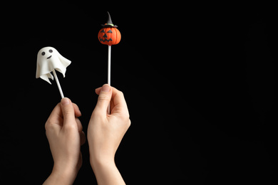 Woman with delicious cake pops and space for text on black background, closeup. Halloween celebration