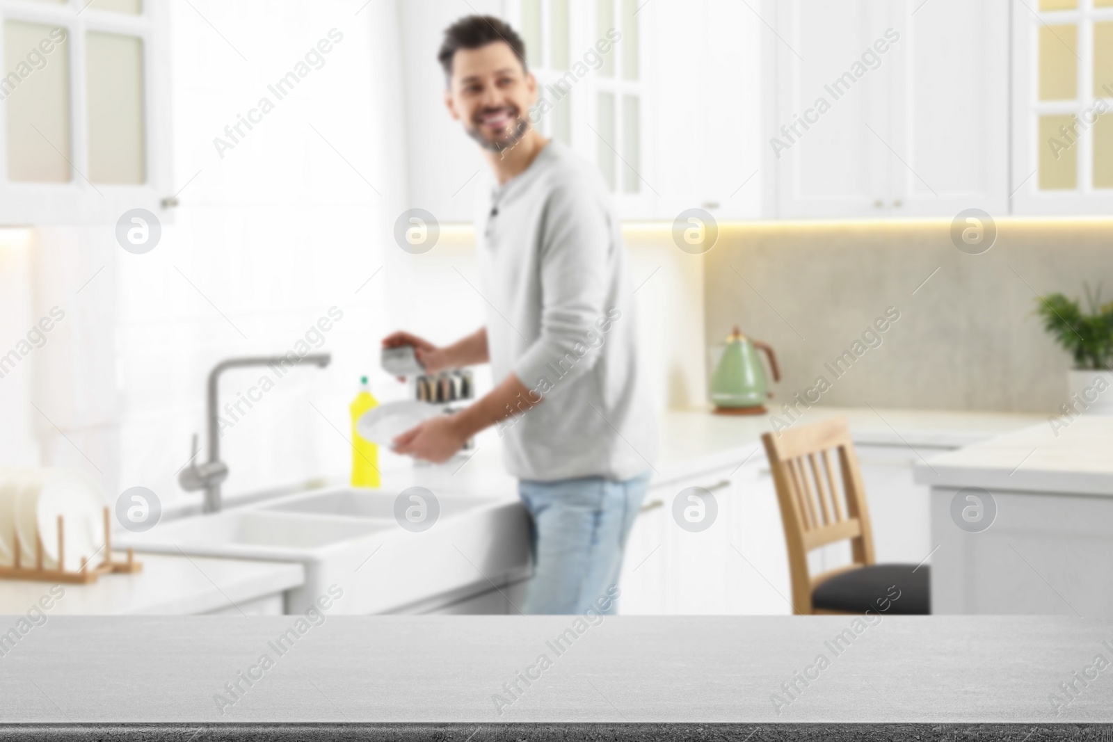 Image of Man doing washing up in kitchen, focus on empty grey stone table