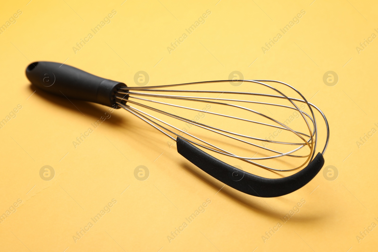Photo of Metal whisk on yellow background, closeup. Kitchen tool