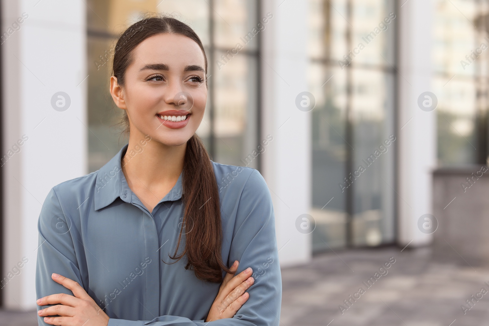 Photo of Portrait of beautiful woman with crossed arms outdoors. Attractive lady smiling and posing for camera. Space for text