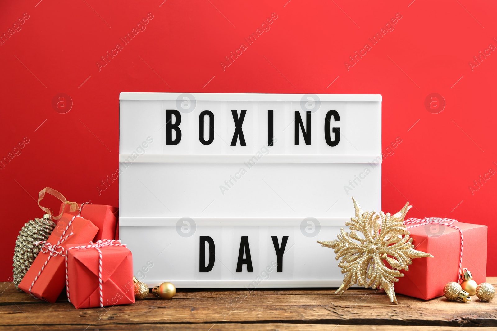 Photo of Composition with Boxing Day sign and Christmas gifts on wooden table against red background
