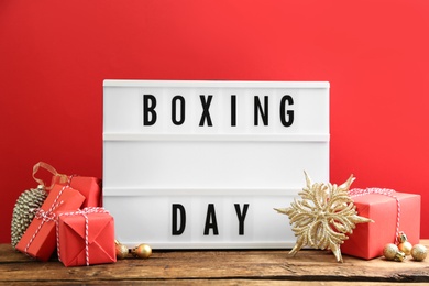 Photo of Composition with Boxing Day sign and Christmas gifts on wooden table against red background
