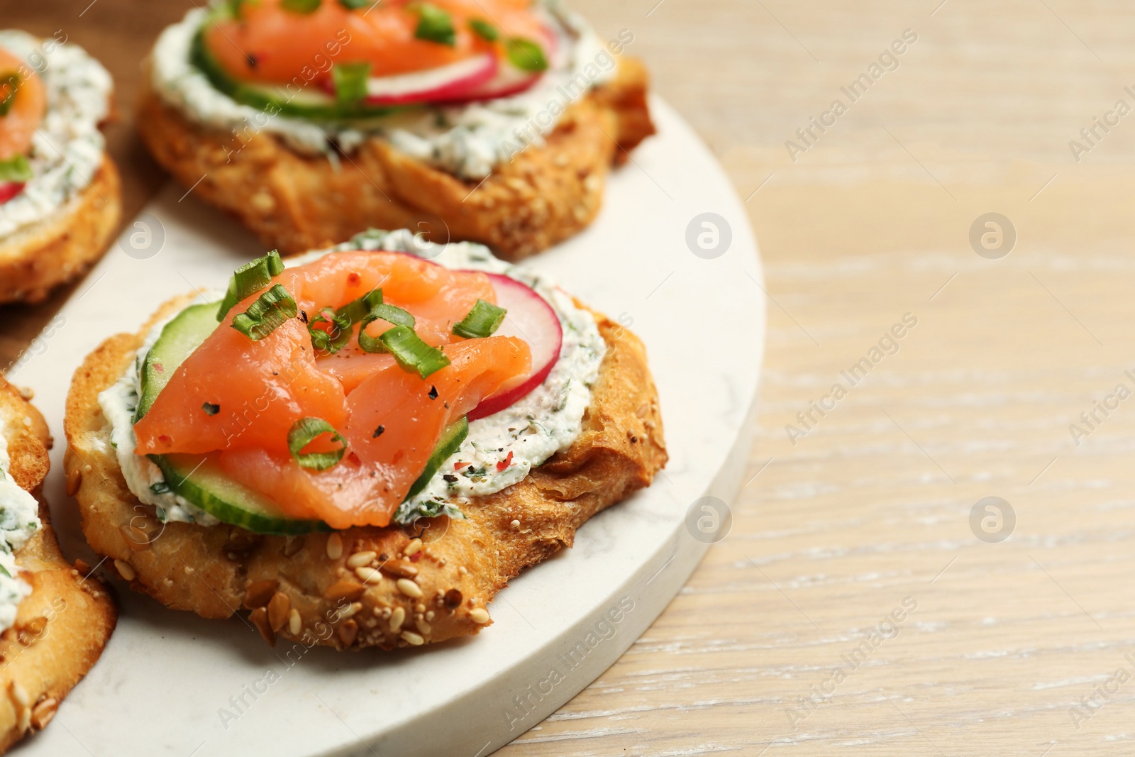 Photo of Tasty canapes with salmon, cucumber, radish and cream cheese on wooden table, closeup. Space for text