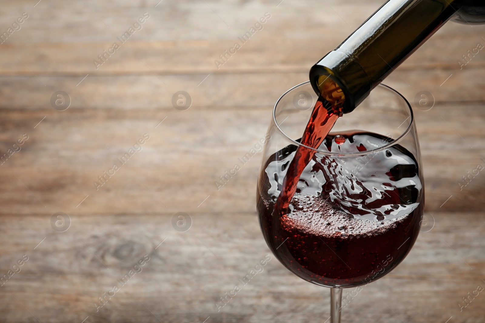 Photo of Pouring red wine from bottle into glass on wooden background. Space for text