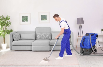 Male worker removing dirt from carpet with professional vacuum cleaner indoors